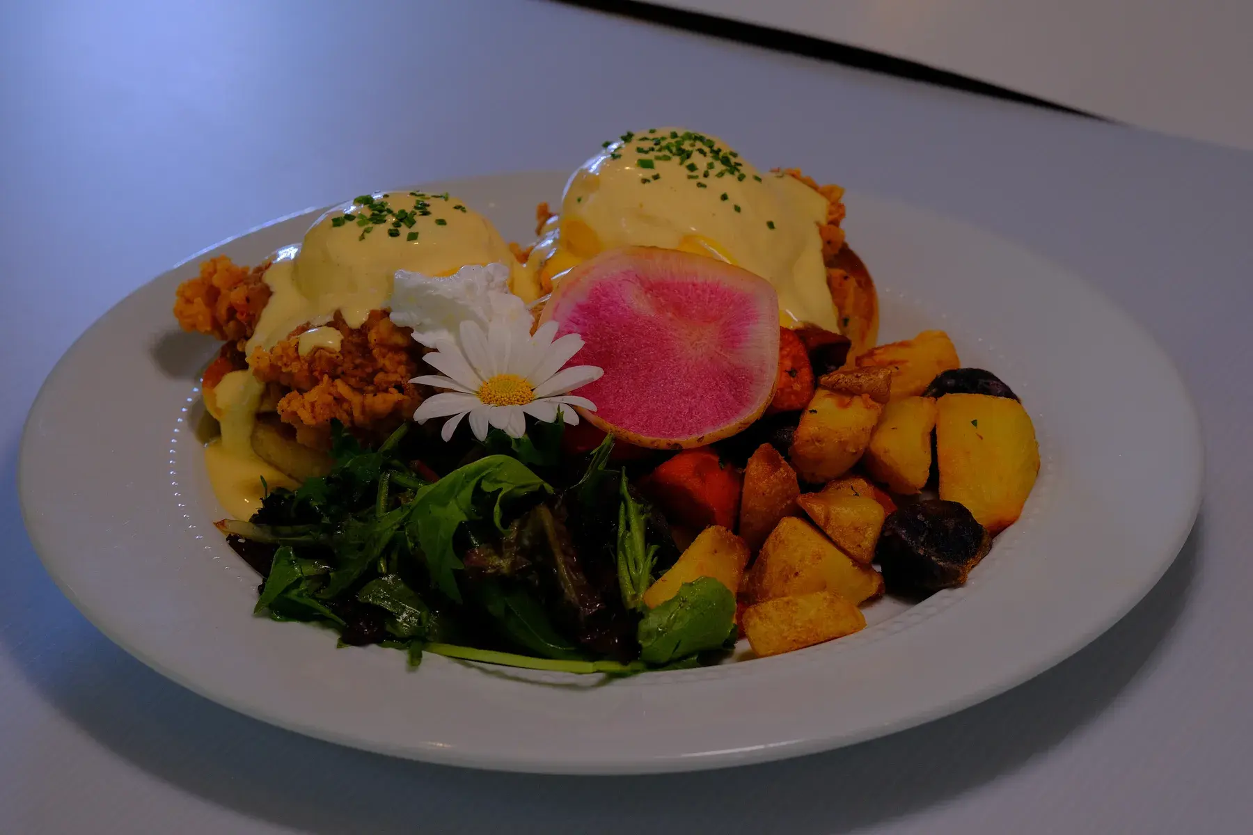 Fried chicken benedict with two poached eggs under hollandaise, breakfast potatoes and salad