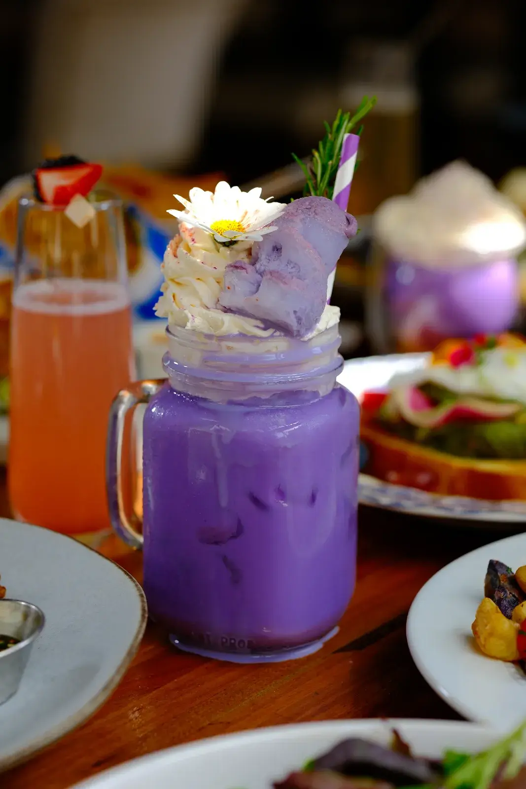 A purple whipped drink in a mason jar beside an orange layered iced drink