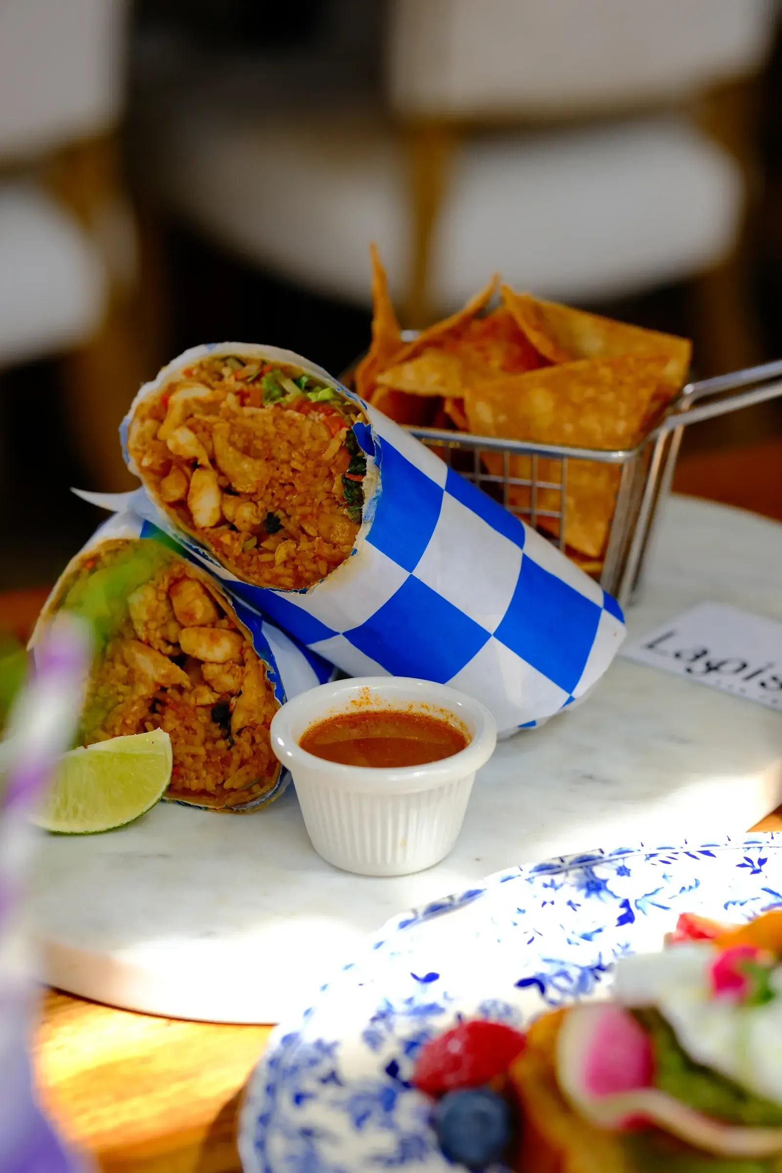A halved burrito in blue-check paper with a basket of tortilla chips and a pot of sauce