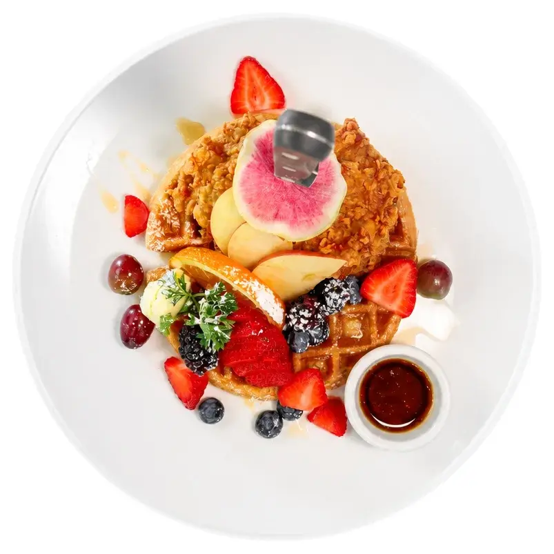 Fried chicken over a waffle with berries and a pot of syrup