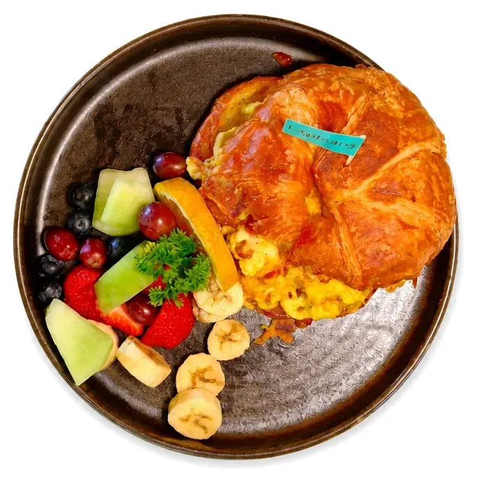 A croissant sandwich with scrambled egg and fresh fruit